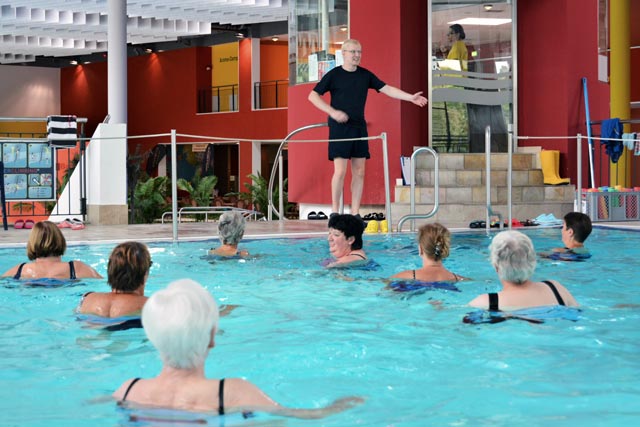 Kursleiter am Beckenrand leitet weibliche Kursteilnehmerinnen im Schwimmbecken an